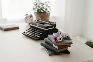 Mesa com relógio, máquina de escrever e livros cobertos de flores.
