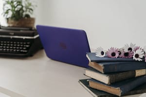 Mesa com computador, máquina de escrever e livros.